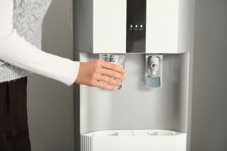 Young businesswoman pouring cold water from cooler in office, closeupの写真素材