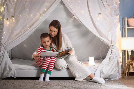 Mother with her little son reading story in hut at homeの写真素材