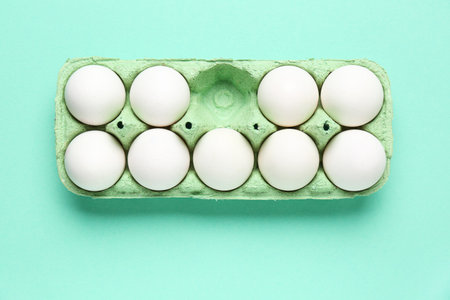 Cardboard holder with raw chicken eggs on turquoise background