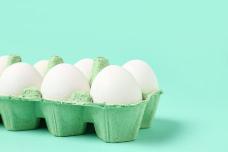 Cardboard holder with raw chicken eggs on turquoise background, closeup