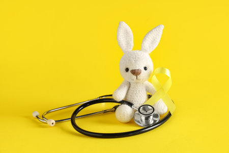 Toy bunny, yellow ribbon and stethoscope on color background. Childhood cancer awareness conceptの写真素材