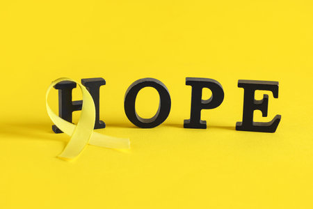 Word HOPE made of black letters and yellow ribbon on color background. Childhood cancer awareness conceptの写真素材