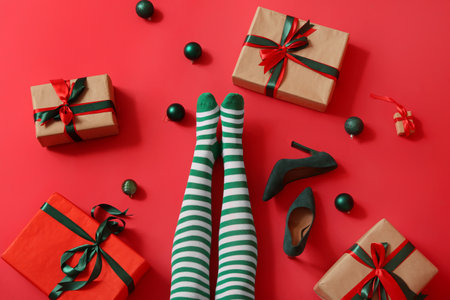 Legs of young woman in striped stockings with gift boxes and Christmas balls on red backgroundの写真素材