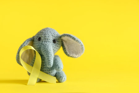 Knitted toy elephant with yellow ribbon on color background. Childhood cancer awareness conceptの写真素材