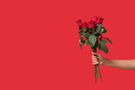 Female hand with bouquet of beautiful red roses on color background. Valentine's day celebrationの写真素材