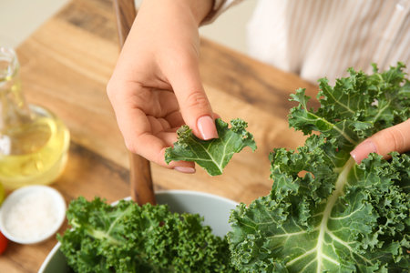 Woman with fresh leaves of kale cabbage on wooden background, closeupの写真素材