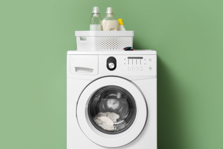 Washing machine with bottles of laundry detergent near green wallの写真素材