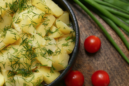 Bowl of tasty potato salad with green onion and tomatoes on wooden boardの写真素材