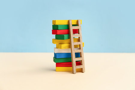 Tower made of colorful building blocks with wooden ladder on color backgroundの写真素材