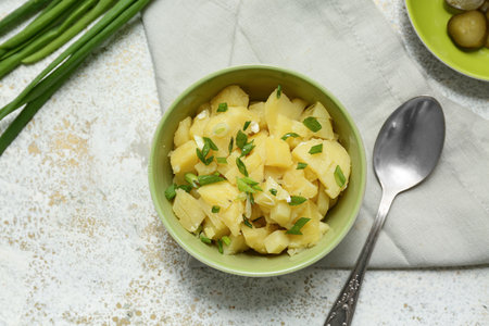 Bowl of tasty potato salad with green onion and spoon on light grunge backgroundの写真素材