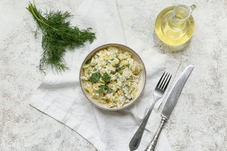Bowl of tasty potato salad with greens, cutlery and oil on light grunge backgroundの写真素材