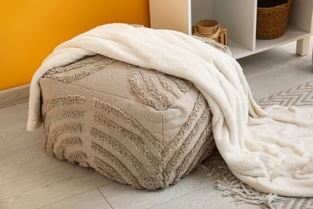 Gray pouf with plaid and shelving unit near yellow wall in roomの写真素材