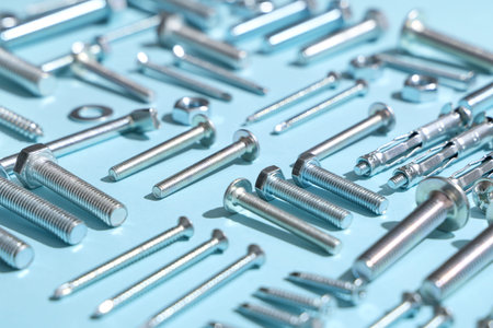 Arrangement of different tap bolts and chrome nuts on blue background, closeup