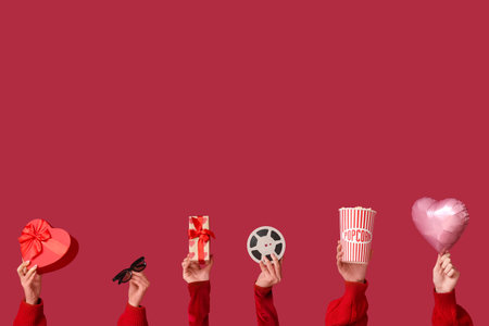 Female hands with gift boxes, film reel, bucket of popcorn, 3D glasses and air balloon in shape of heart on red background. Valentine's Day celebrationの写真素材