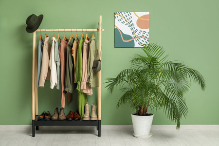 Rack with clothes with stand for shoes and houseplant near green wallの写真素材