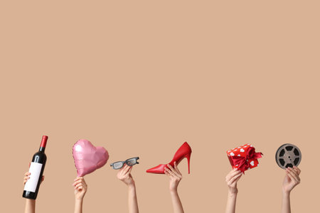 Female hands with bottle of wine, heeled shoe, 3D glasses, film reel, gift box and air balloon in shape of heart on beige background. Valentine's Day celebrationの写真素材