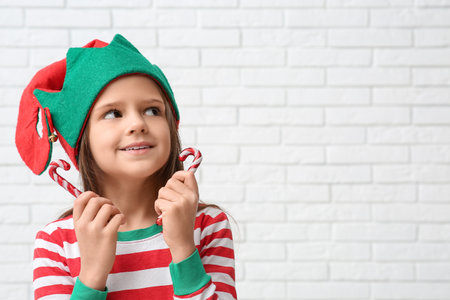 Cute little girl in elf costume with candy canes near white brick wall. Christmas celebrationの写真素材
