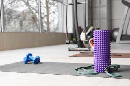 Foam roller with stretch band and dumbbells on mat at gymの写真素材