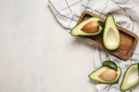 Wooden tray with halves of fresh ripe avocados on white background