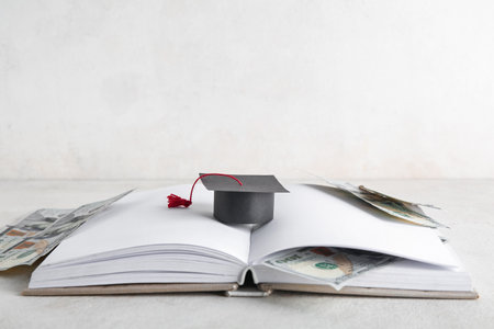 Open book, small graduation hat and dollar banknotes on light background. Student loan conceptの写真素材