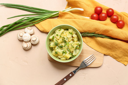 Bowl of tasty potato salad with dill, green onion, mushrooms and tomatoes on beige backgroundの写真素材