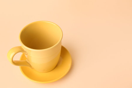 Yellow ceramic cup and saucer on beige background