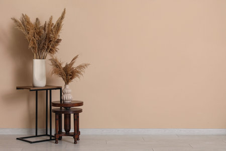 Pampas grass in vases on stands near brown wall in room
