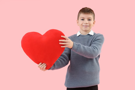 Cute little happy boy with heart-shaped pillow on pink background. Valentine's Day celebrationの写真素材