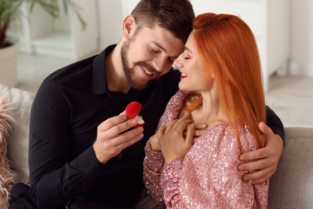 Young man with engagement ring proposing to his happy girlfriend at home. Valentine's Day celebrationの写真素材