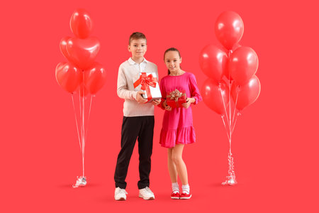 Cute little happy children with balloons and gift boxes on red background. Valentine's Day celebrationの写真素材