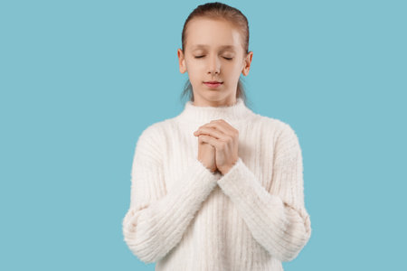 Teenage girl praying on blue backgroundの写真素材