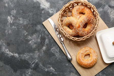 Wicker bowl of tasty bagels with sesame seeds on black background
