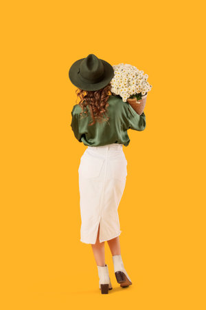 Fashionable young woman with beautiful chrysanthemum flowers on yellow background, back viewの写真素材