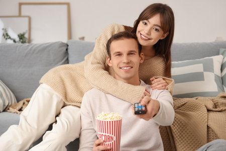 Young couple with popcorn watching TV at homeの写真素材