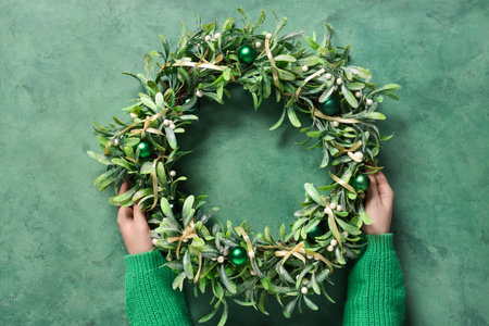 Female hands with beautiful mistletoe wreath on grunge green backgroundの写真素材