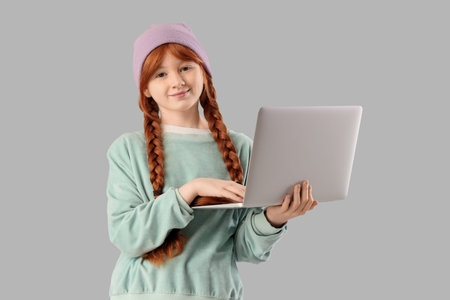 Teenage redhead girl using laptop on light background