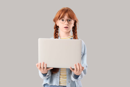 Shocked teenage redhead girl with laptop on light backgroundの写真素材