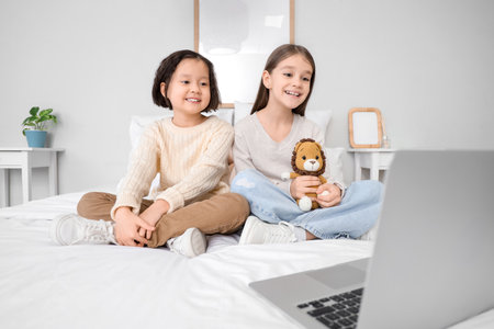 Cute girls watching cartoons on laptop in bedroomの写真素材