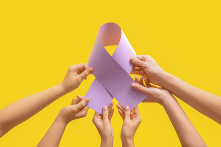 Hands holding paper awareness ribbon on yellow backgroundの写真素材