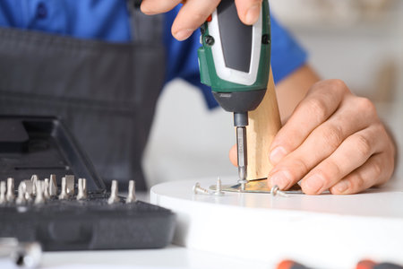 Male carpenter tightening screw in wooden table with electric screwdriver, closeupの写真素材