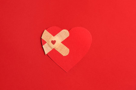 Red paper heart with medical patches on color background. Valentine's Day celebrationの写真素材