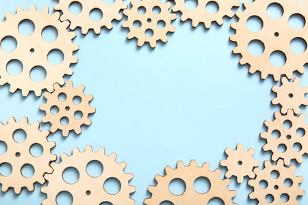Frame made of wooden gears on light blue background