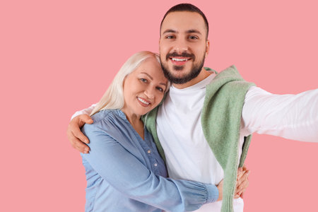 Young man hugging his mother and taking selfie on pink backgroundの写真素材