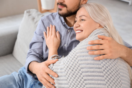 Young man hugging his mother with plaid at home, closeupの写真素材