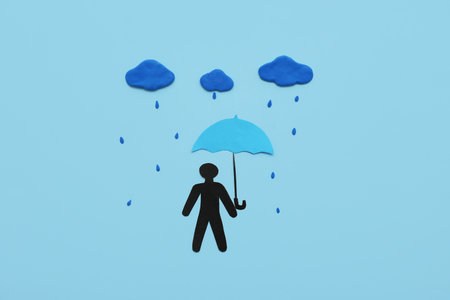 Paper human figure with umbrella, clouds and rain drops on blue backgroundの写真素材