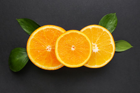 Slices of fresh ripe orange and leaves on black backgroundの写真素材