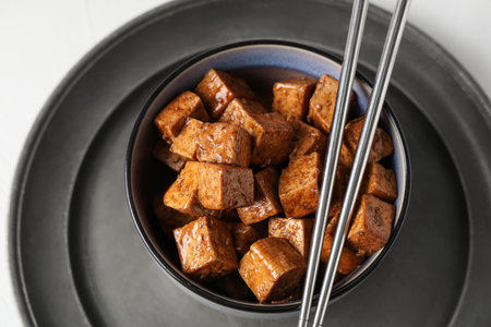 Bowl with pieces of fried tofu cheese and metal chopsticks on white backgroundの写真素材
