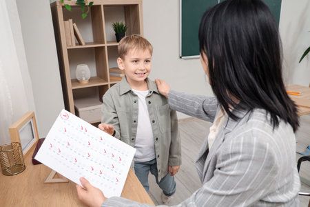 Cute schoolboy receiving answer sheet with A grade from teacher in classroomの写真素材