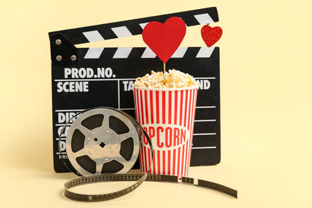 Bucket of popcorn with hearts, movie clapper and film reel on yellow background. Valentine's Day celebrationの写真素材