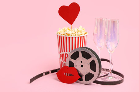Bucket of popcorn with film reel and champagne glasses on pink background. Valentine's Day celebrationの写真素材